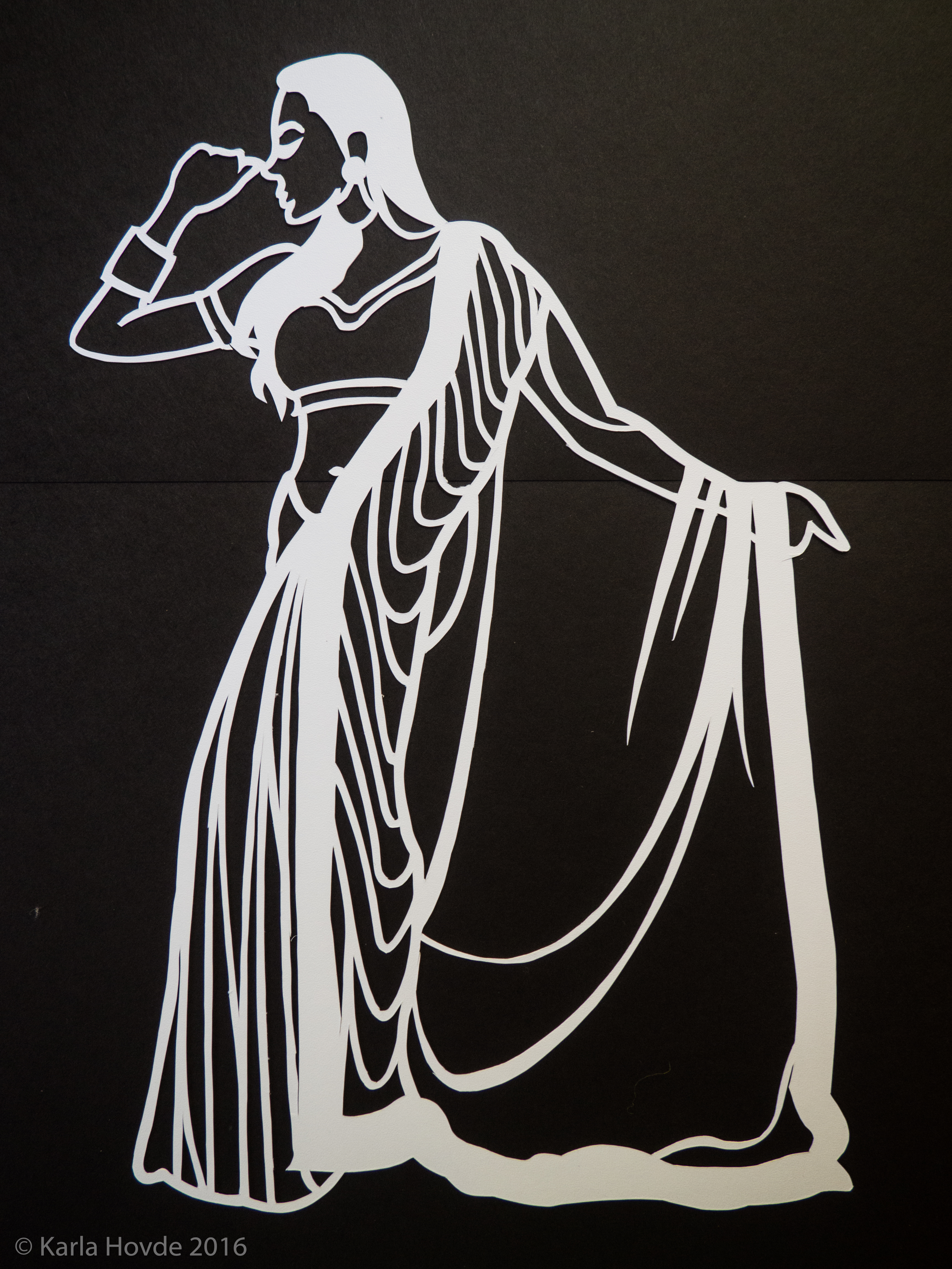Paper cutting art in white paper shows stylized woman wearing a sari and dancing.